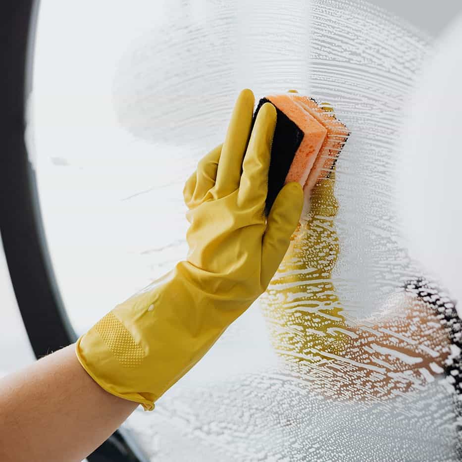 Gele schoonmaakhandschoen reinigt een glazen oppervlak met een spons.